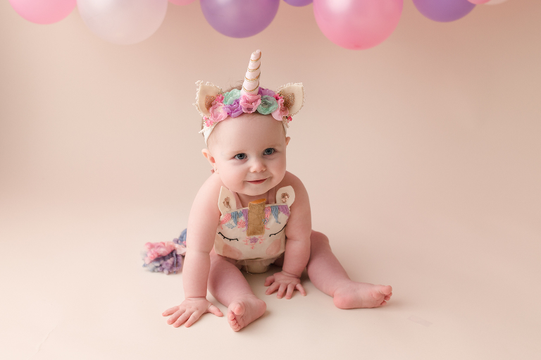 smiling one year old baby girl in unicorn outfit